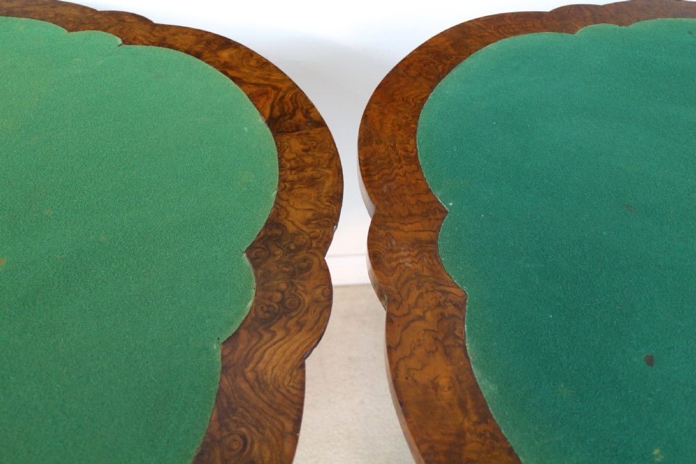 A pair of Victorian burr walnut fold-over card tables featuring shaped demi-lune tops, carved aprons, central turned pedestals, and carved quadform legs with castors. View XVII