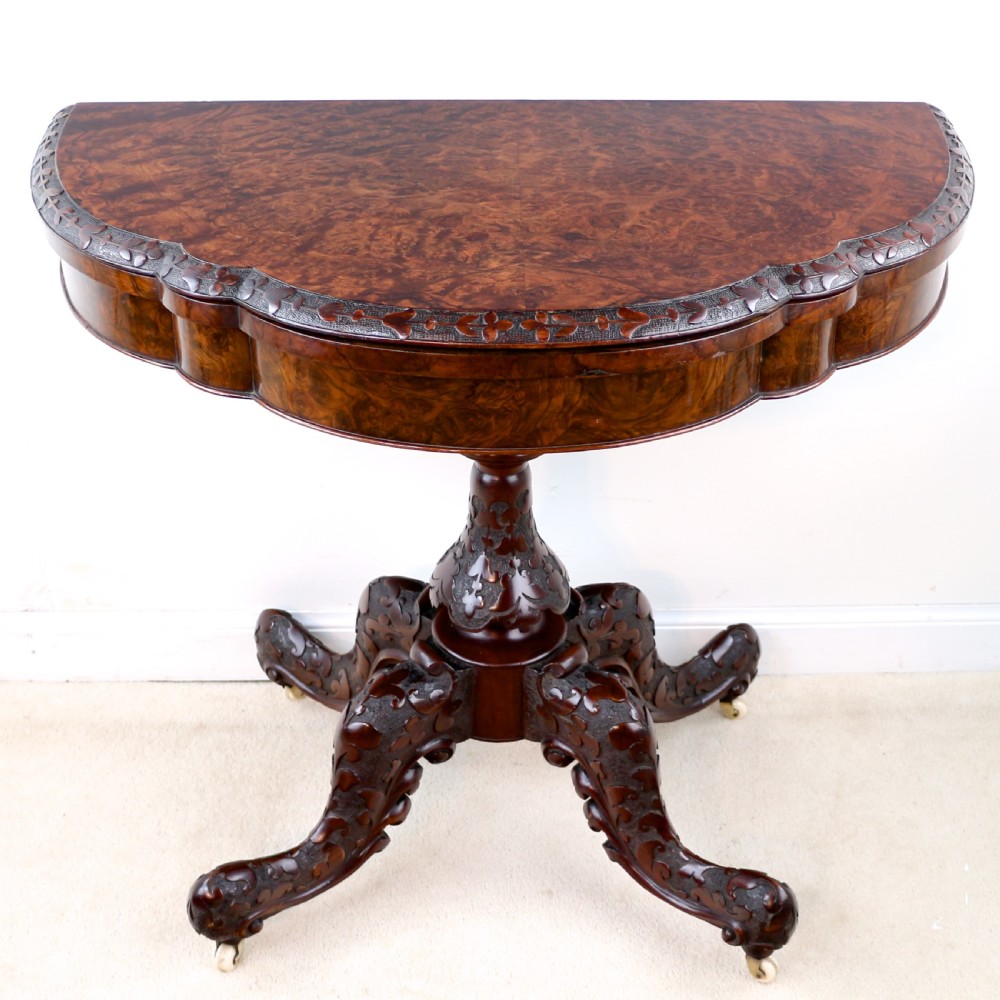 A pair of Victorian burr walnut fold-over card tables featuring shaped demi-lune tops, carved aprons, central turned pedestals, and carved quadform legs with castors. View XIX