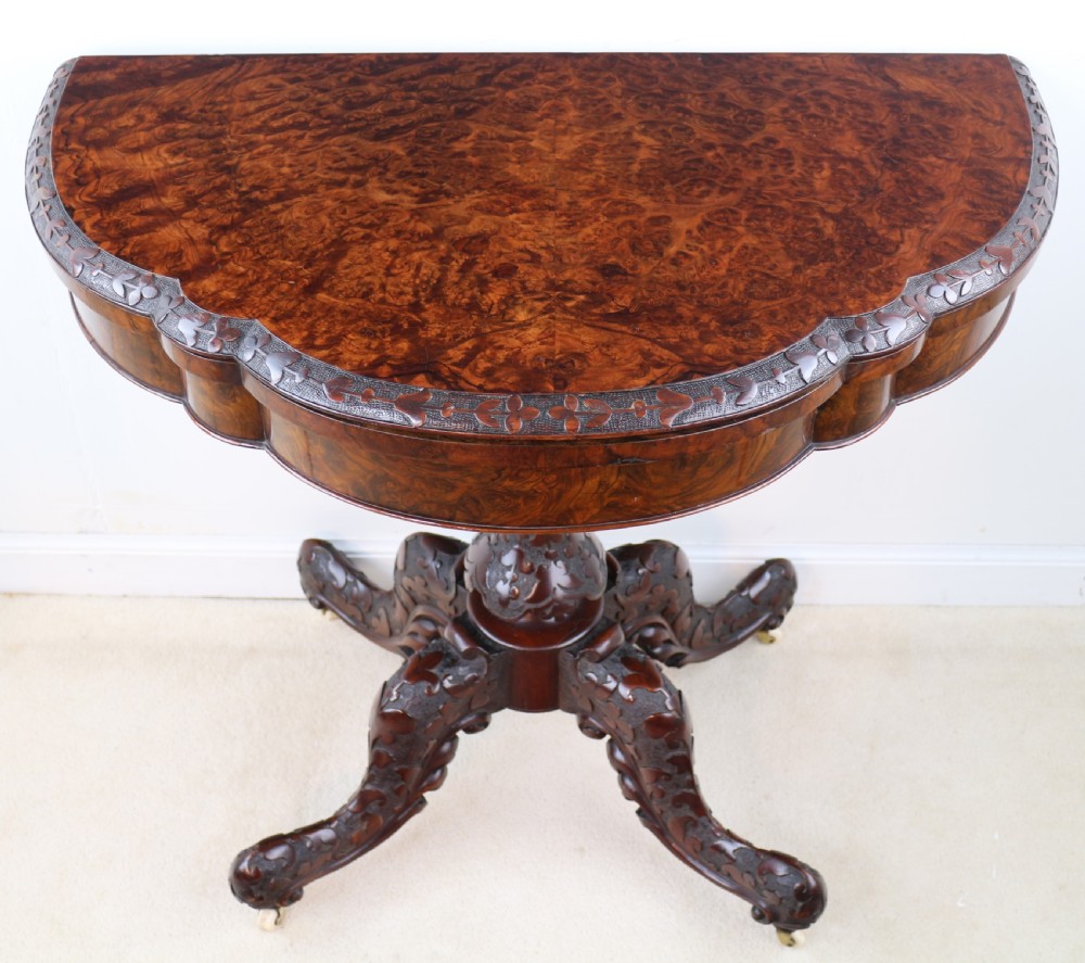 A pair of Victorian burr walnut fold-over card tables featuring shaped demi-lune tops, carved aprons, central turned pedestals, and carved quadform legs with castors. View XX