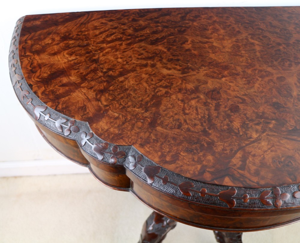 A pair of Victorian burr walnut fold-over card tables featuring shaped demi-lune tops, carved aprons, central turned pedestals, and carved quadform legs with castors. View XXI
