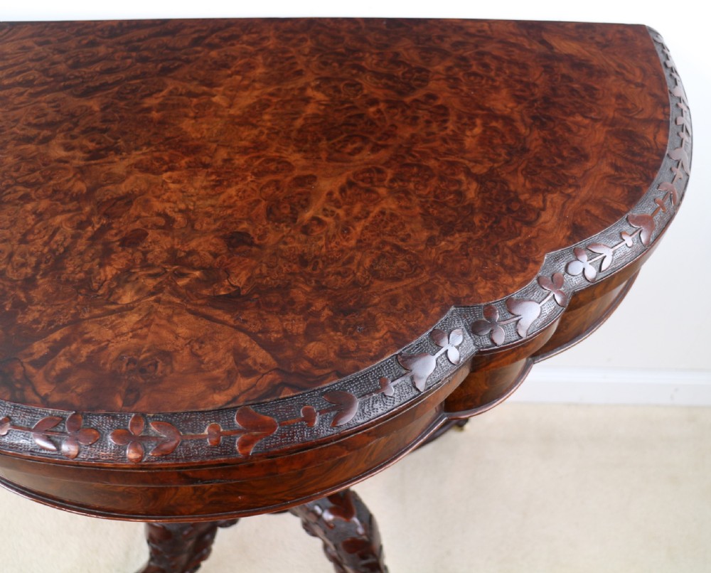 A pair of Victorian burr walnut fold-over card tables featuring shaped demi-lune tops, carved aprons, central turned pedestals, and carved quadform legs with castors. View XXII
