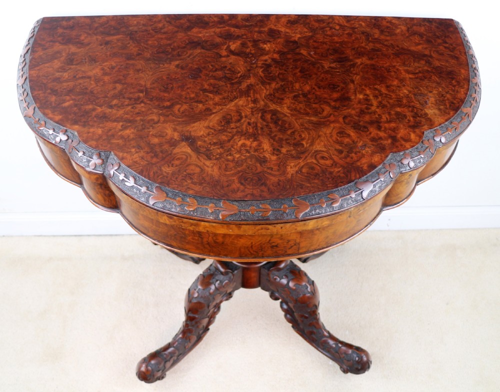 A pair of Victorian burr walnut fold-over card tables featuring shaped demi-lune tops, carved aprons, central turned pedestals, and carved quadform legs with castors. View XXVI