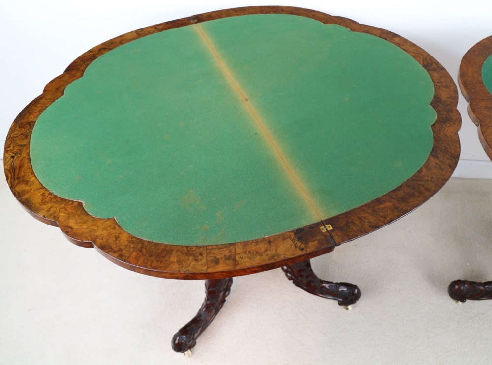 A pair of Victorian burr walnut fold-over card tables featuring shaped demi-lune tops, carved aprons, central turned pedestals, and carved quadform legs with castors. View XXVII