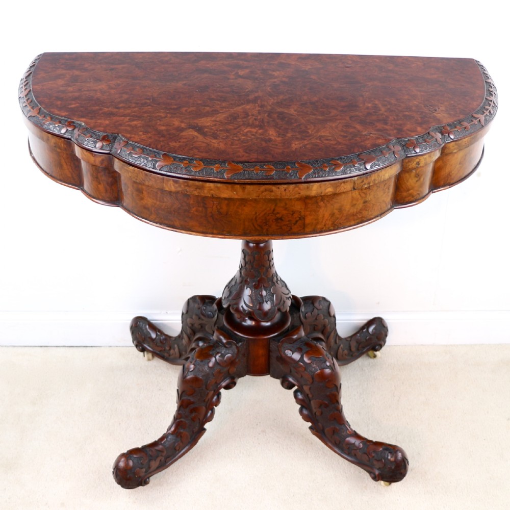 A pair of Victorian burr walnut fold-over card tables featuring shaped demi-lune tops, carved aprons, central turned pedestals, and carved quadform legs with castors. View XXXI