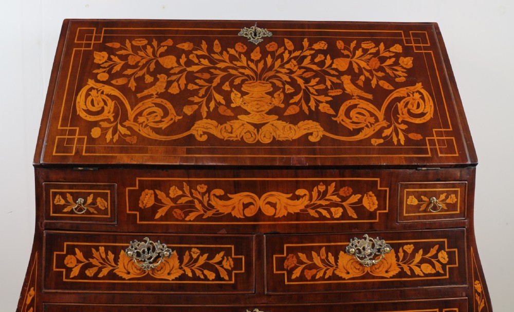 A 19th-century Dutch walnut bombe bureau decorated with intricate floral marquetry, featuring a slant front and curved drawers with brass handles. View V