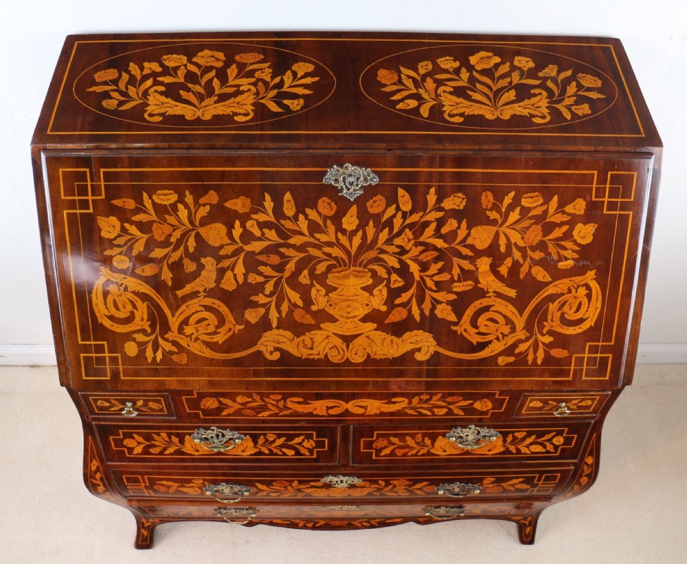 A 19th-century Dutch walnut bombe bureau decorated with intricate floral marquetry, featuring a slant front and curved drawers with brass handles. View VII