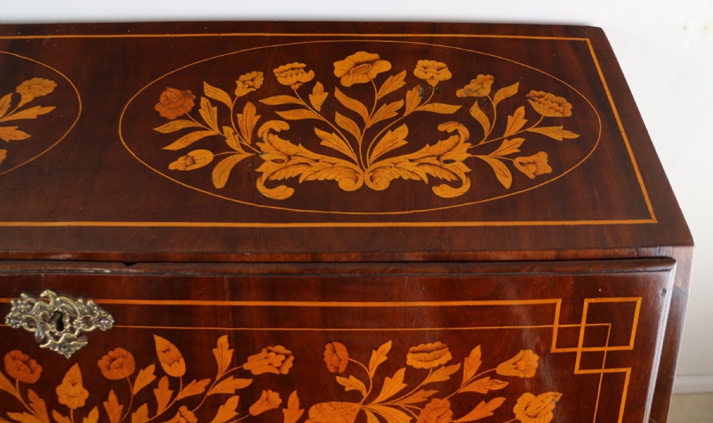 A 19th-century Dutch walnut bombe bureau decorated with intricate floral marquetry, featuring a slant front and curved drawers with brass handles. View IX