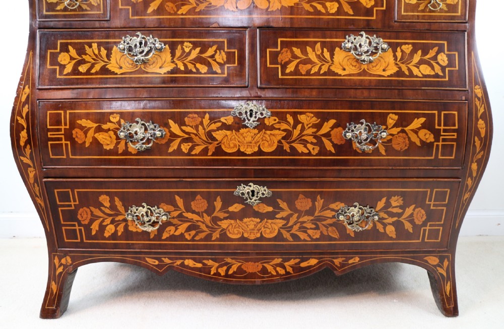 A 19th-century Dutch walnut bombe bureau decorated with intricate floral marquetry, featuring a slant front and curved drawers with brass handles. View X