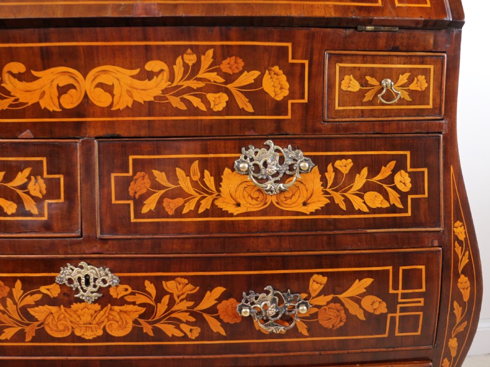 A 19th-century Dutch walnut bombe bureau decorated with intricate floral marquetry, featuring a slant front and curved drawers with brass handles. View XII