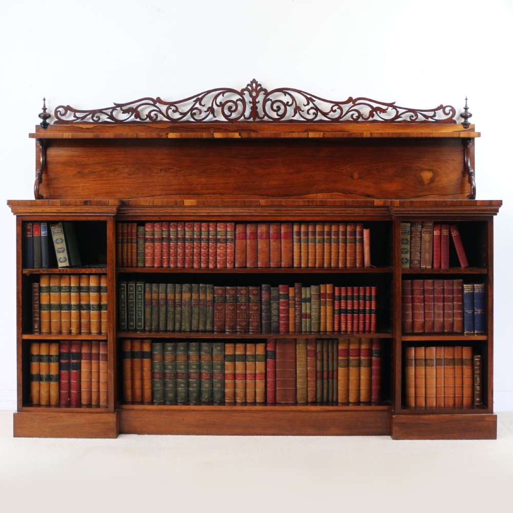An antique Regency open rosewood bookcase featuring an inverted breakfront profile, multi-tier shelving, and an intricately carved fretwork gallery. View II