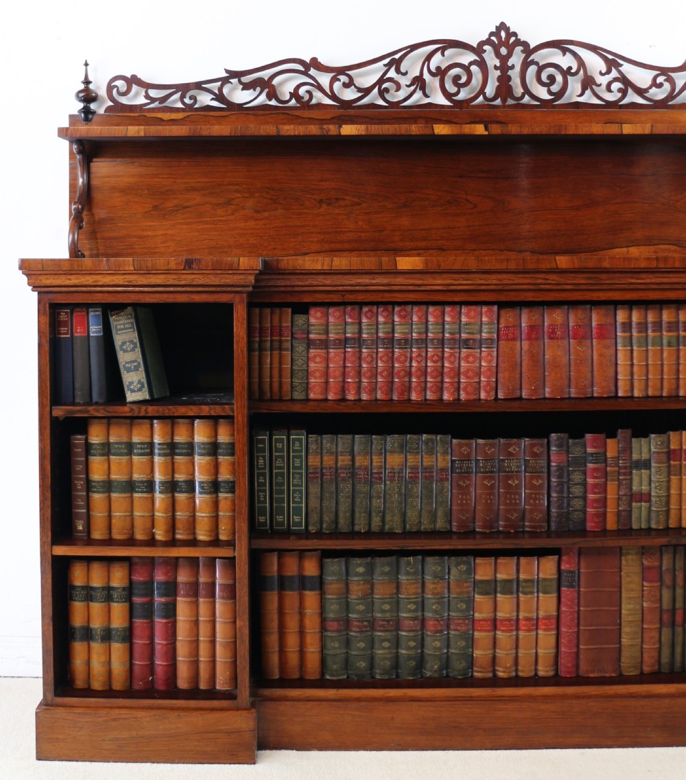 An antique Regency open rosewood bookcase featuring an inverted breakfront profile, multi-tier shelving, and an intricately carved fretwork gallery. View V