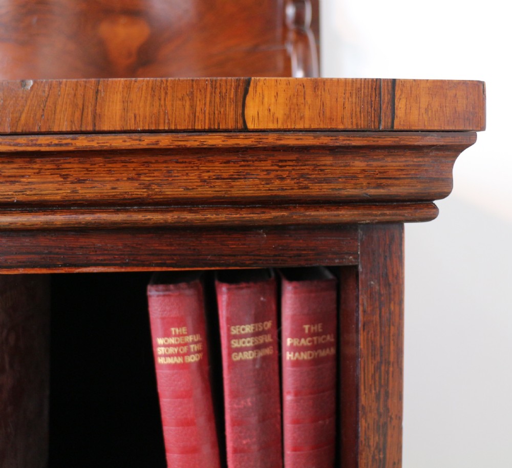 An antique Regency open rosewood bookcase featuring an inverted breakfront profile, multi-tier shelving, and an intricately carved fretwork gallery. View VI