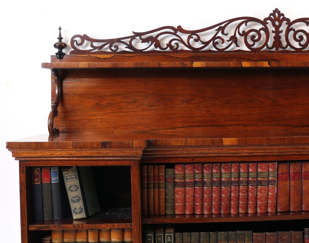 An antique Regency open rosewood bookcase featuring an inverted breakfront profile, multi-tier shelving, and an intricately carved fretwork gallery. View VII