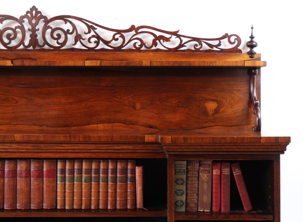 An antique Regency open rosewood bookcase featuring an inverted breakfront profile, multi-tier shelving, and an intricately carved fretwork gallery. View IX