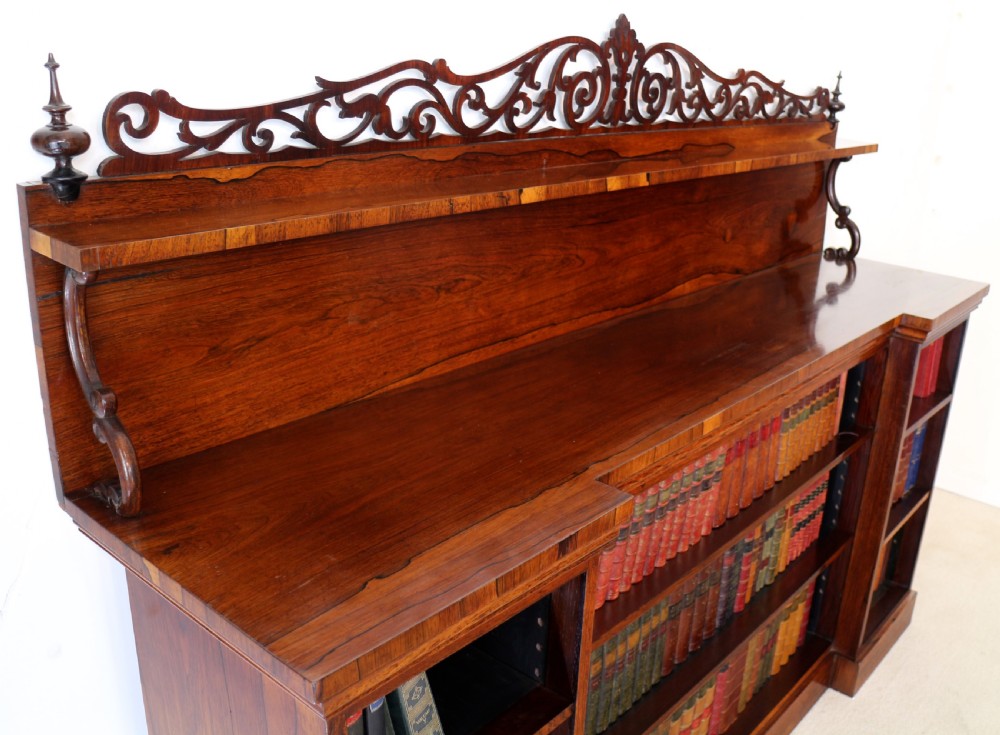 An antique Regency open rosewood bookcase featuring an inverted breakfront profile, multi-tier shelving, and an intricately carved fretwork gallery. View XII