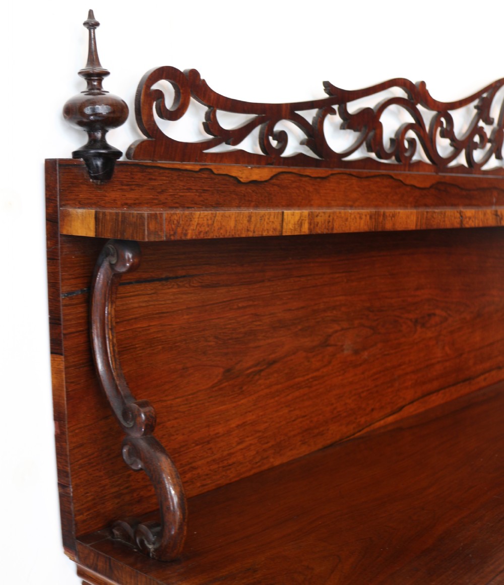 An antique Regency open rosewood bookcase featuring an inverted breakfront profile, multi-tier shelving, and an intricately carved fretwork gallery. View XIV