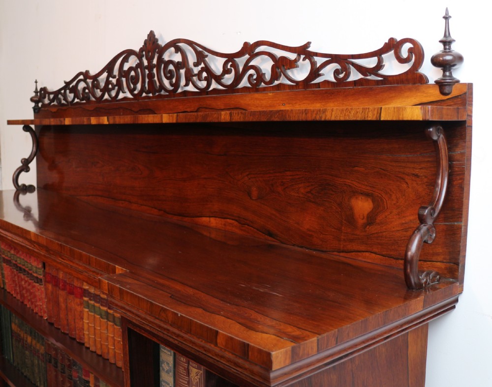 An antique Regency open rosewood bookcase featuring an inverted breakfront profile, multi-tier shelving, and an intricately carved fretwork gallery. View XXVII