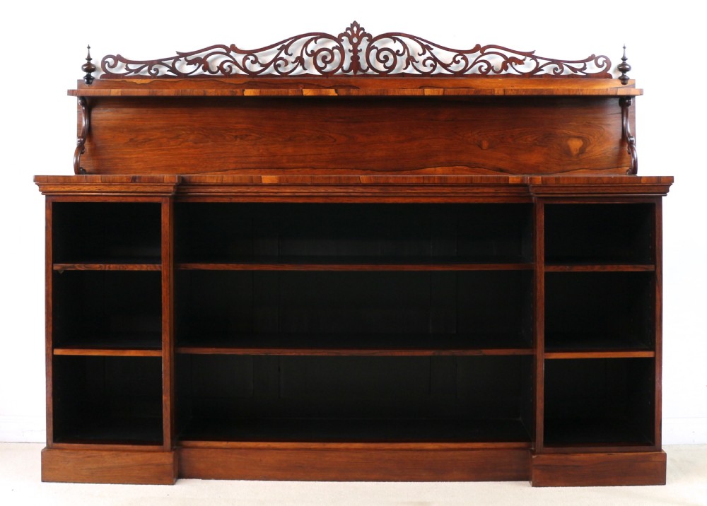 An antique Regency open rosewood bookcase featuring an inverted breakfront profile, multi-tier shelving, and an intricately carved fretwork gallery. View XXVIII