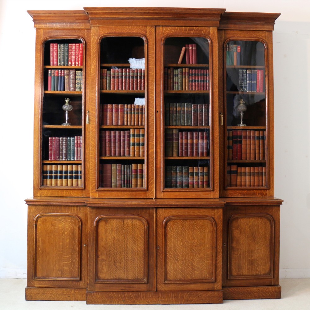 A large William IV golden oak breakfront bookcase featuring glazed upper doors above panelled wooden cupboard doors.