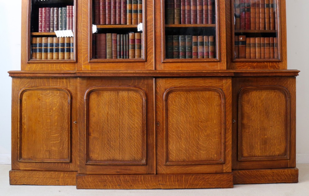 A large William IV golden oak breakfront bookcase featuring glazed upper doors above panelled wooden cupboard doors. View III