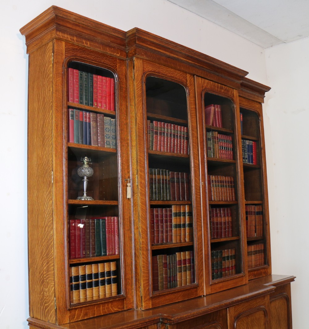A large William IV golden oak breakfront bookcase featuring glazed upper doors above panelled wooden cupboard doors. View VI