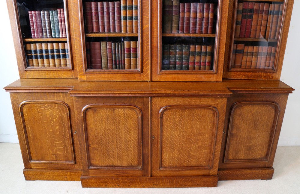 A large William IV golden oak breakfront bookcase featuring glazed upper doors above panelled wooden cupboard doors. View VII