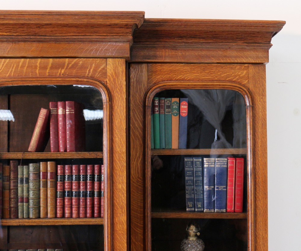 A large William IV golden oak breakfront bookcase featuring glazed upper doors above panelled wooden cupboard doors. View X