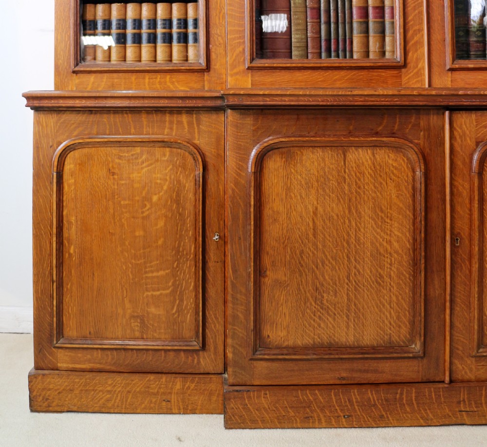 A large William IV golden oak breakfront bookcase featuring glazed upper doors above panelled wooden cupboard doors. View XI