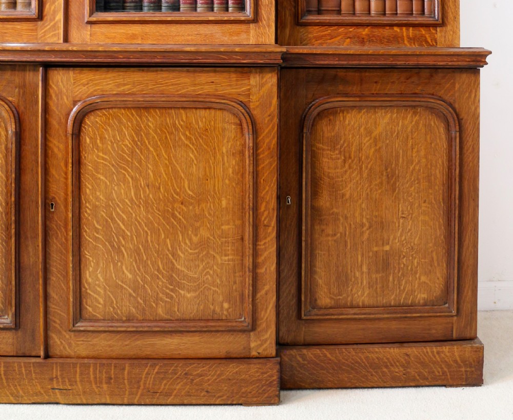 A large William IV golden oak breakfront bookcase featuring glazed upper doors above panelled wooden cupboard doors. View XII