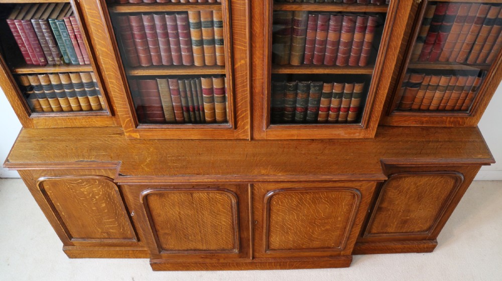 A large William IV golden oak breakfront bookcase featuring glazed upper doors above panelled wooden cupboard doors. View XV