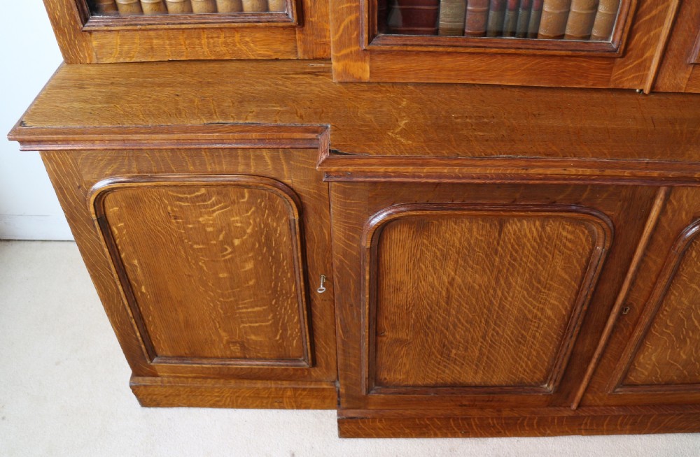 A large William IV golden oak breakfront bookcase featuring glazed upper doors above panelled wooden cupboard doors. View XVI