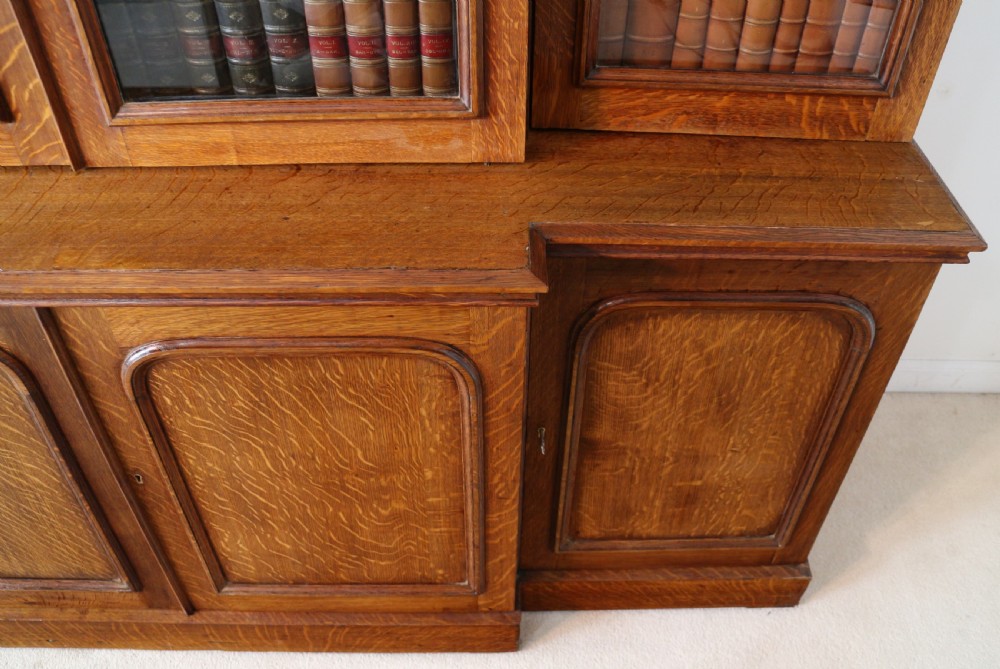 A large William IV golden oak breakfront bookcase featuring glazed upper doors above panelled wooden cupboard doors. View XVII