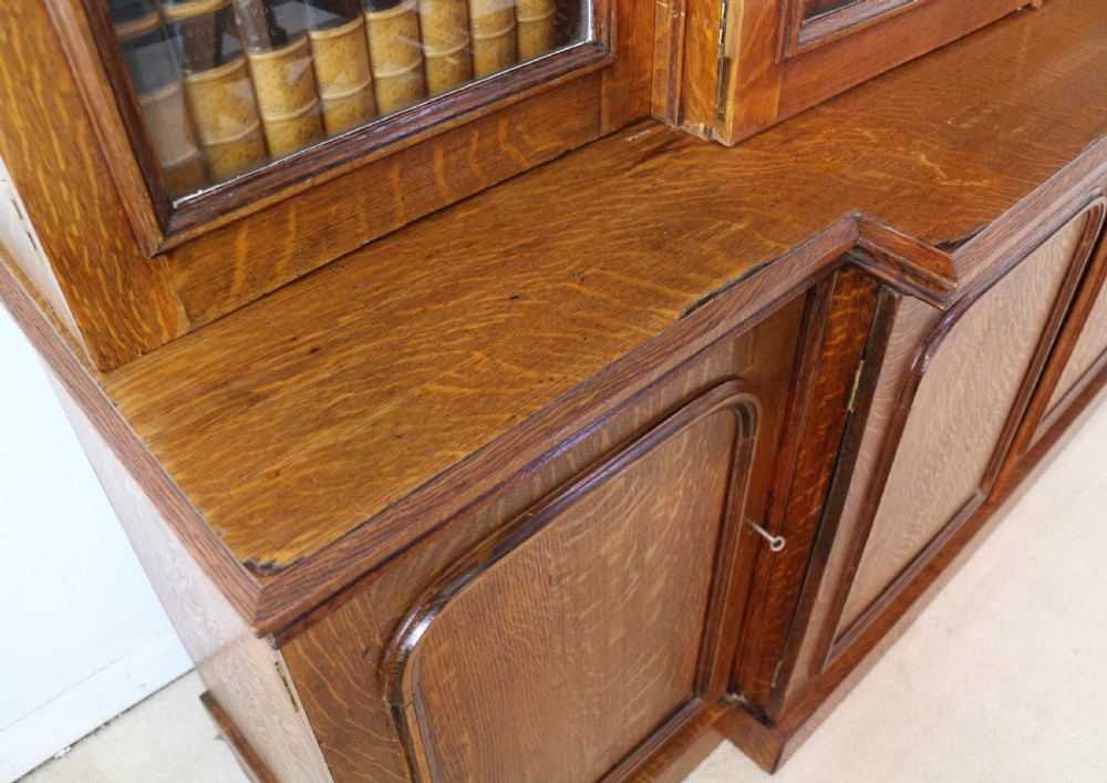 A large William IV golden oak breakfront bookcase featuring glazed upper doors above panelled wooden cupboard doors. View XVIII