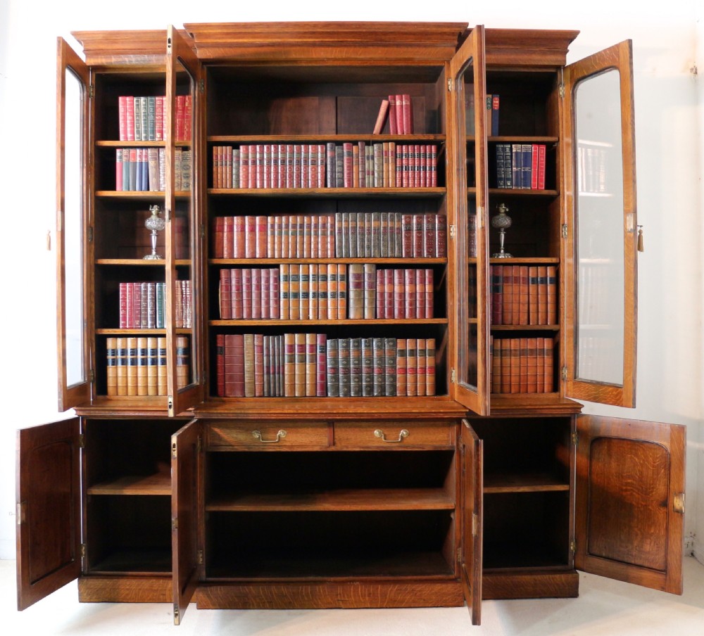 A large William IV golden oak breakfront bookcase featuring glazed upper doors above panelled wooden cupboard doors. View XX