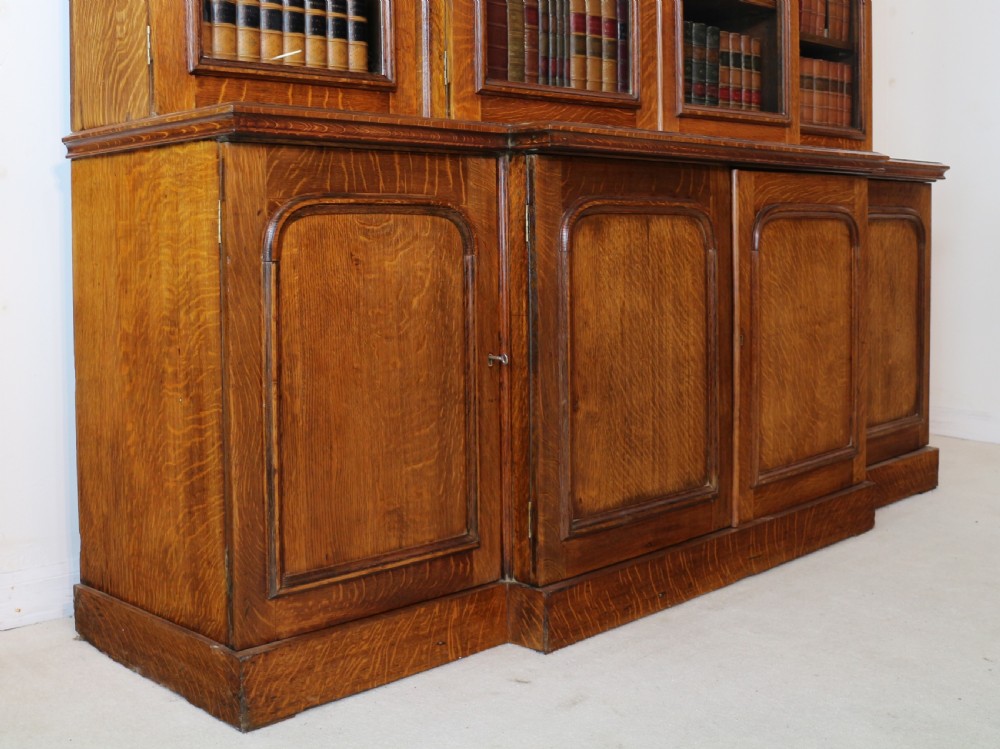 A large William IV golden oak breakfront bookcase featuring glazed upper doors above panelled wooden cupboard doors. View XXVIII
