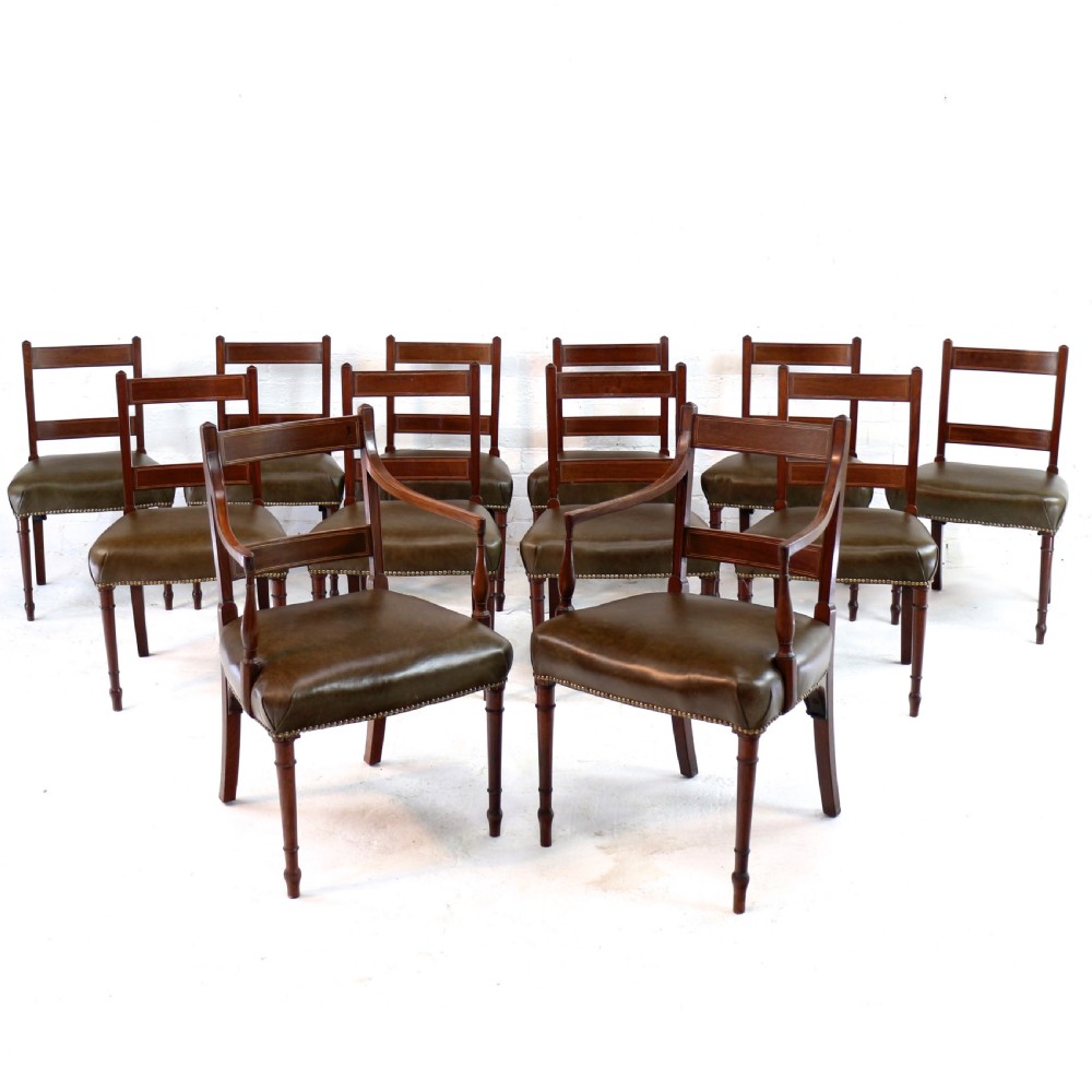 A set of twelve George III mahogany dining chairs featuring rectangular bar-back cresting rails with string inlay, green leather upholstered seats with stud detailing, and turned front legs.