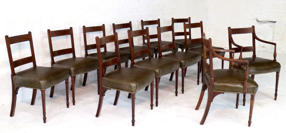 A set of twelve George III mahogany dining chairs featuring rectangular bar-back cresting rails with string inlay, green leather upholstered seats with stud detailing, and turned front legs. View II