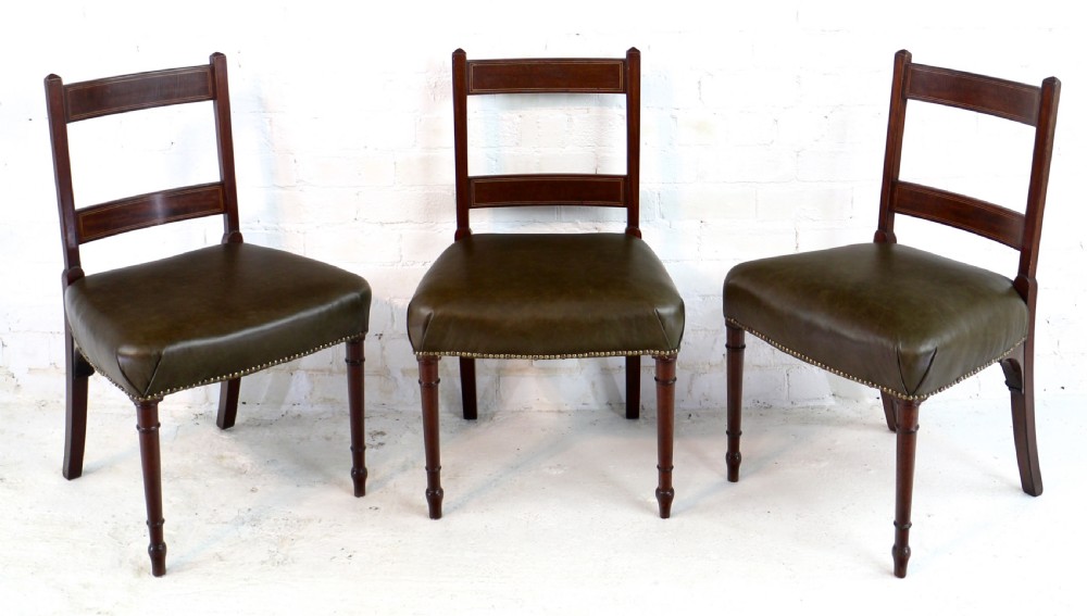 A set of twelve George III mahogany dining chairs featuring rectangular bar-back cresting rails with string inlay, green leather upholstered seats with stud detailing, and turned front legs. View V