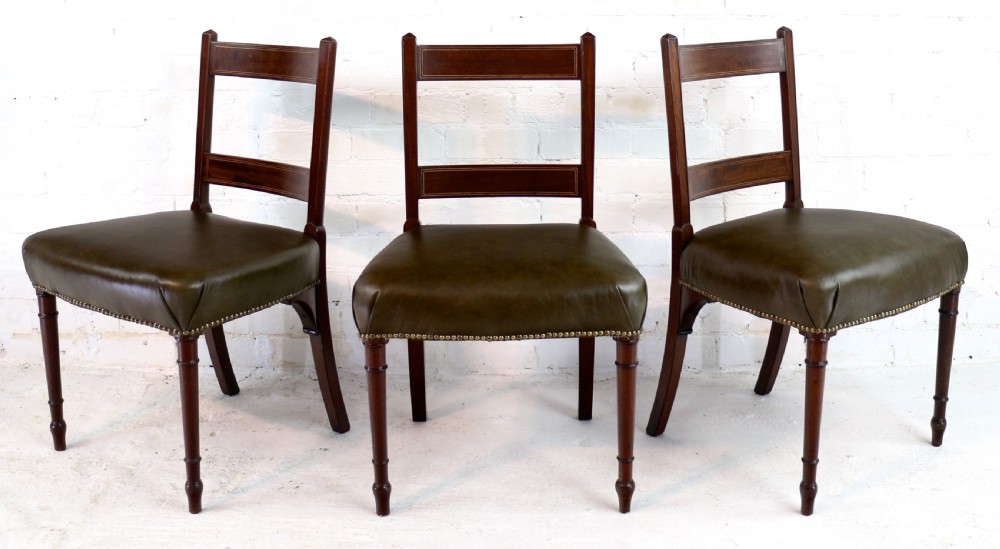 A set of twelve George III mahogany dining chairs featuring rectangular bar-back cresting rails with string inlay, green leather upholstered seats with stud detailing, and turned front legs. View VII