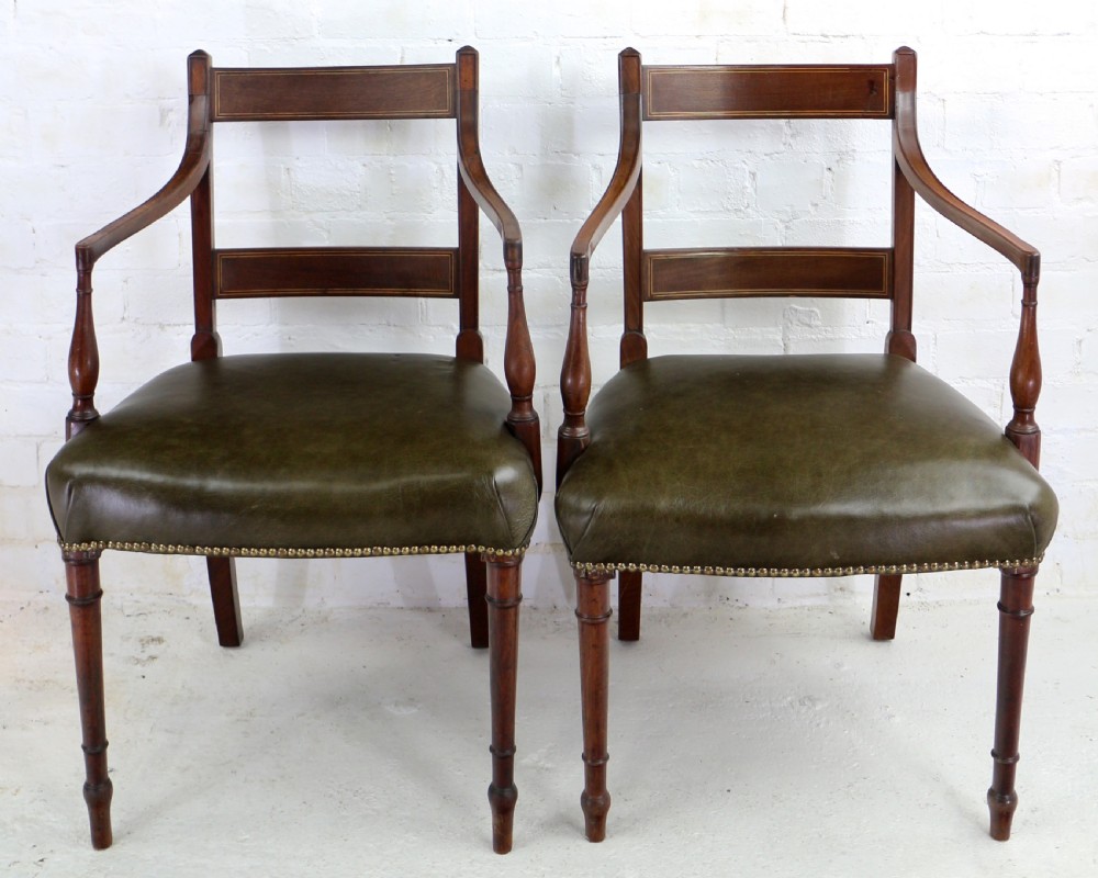 A set of twelve George III mahogany dining chairs featuring rectangular bar-back cresting rails with string inlay, green leather upholstered seats with stud detailing, and turned front legs. View X