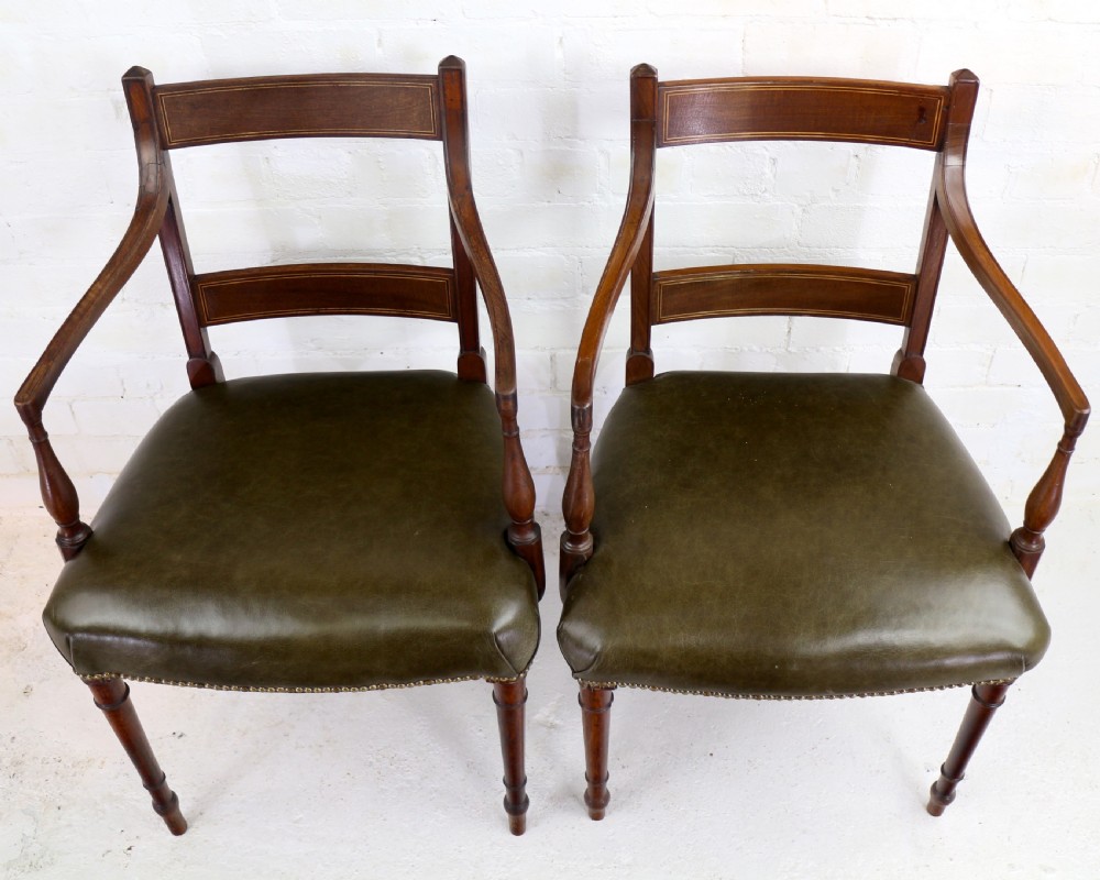 A set of twelve George III mahogany dining chairs featuring rectangular bar-back cresting rails with string inlay, green leather upholstered seats with stud detailing, and turned front legs. View XII