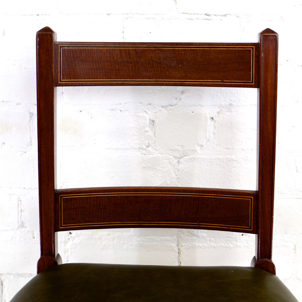 A set of twelve George III mahogany dining chairs featuring rectangular bar-back cresting rails with string inlay, green leather upholstered seats with stud detailing, and turned front legs. View XIV