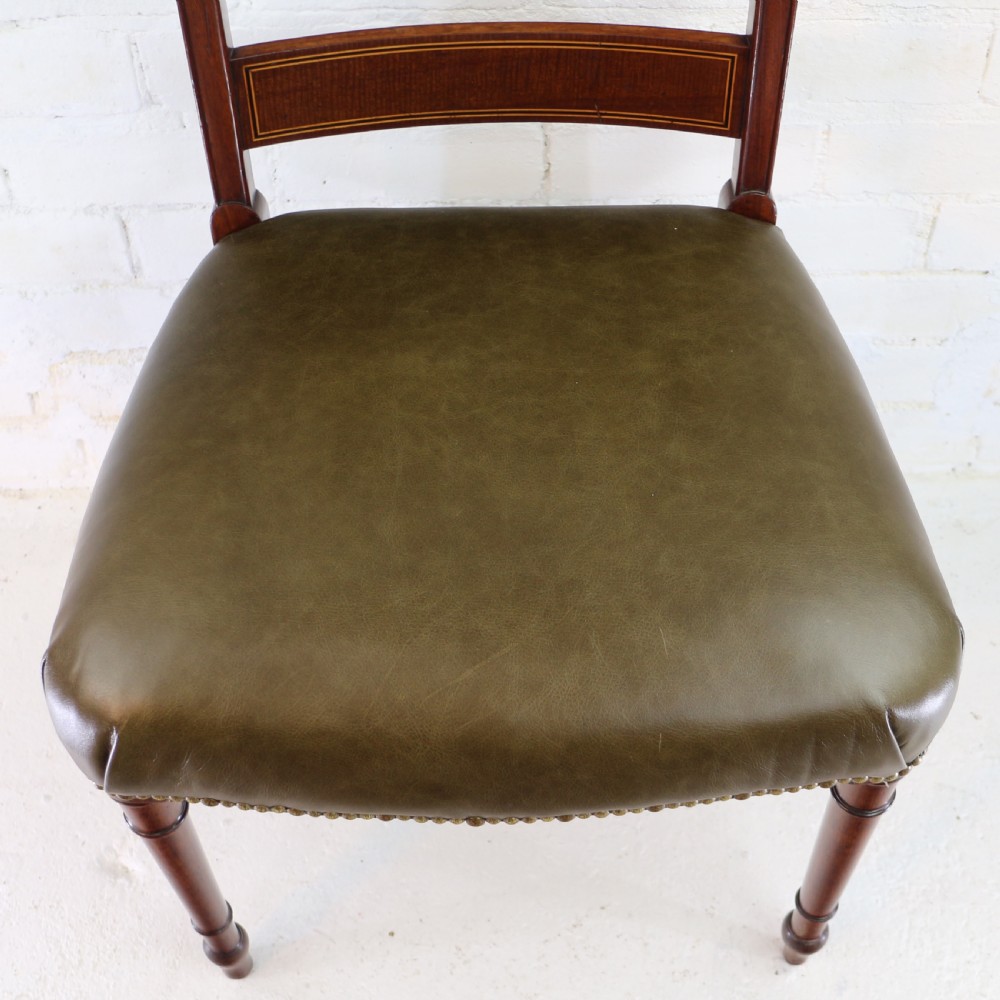 A set of twelve George III mahogany dining chairs featuring rectangular bar-back cresting rails with string inlay, green leather upholstered seats with stud detailing, and turned front legs. View XVII