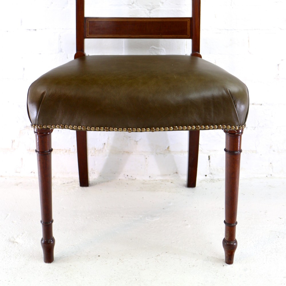 A set of twelve George III mahogany dining chairs featuring rectangular bar-back cresting rails with string inlay, green leather upholstered seats with stud detailing, and turned front legs. View XVIII