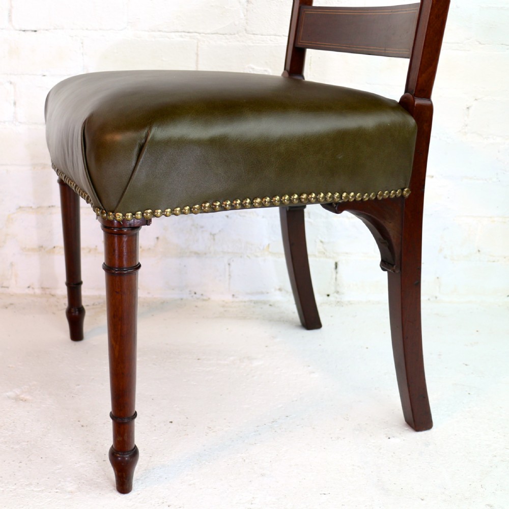 A set of twelve George III mahogany dining chairs featuring rectangular bar-back cresting rails with string inlay, green leather upholstered seats with stud detailing, and turned front legs. View XIX