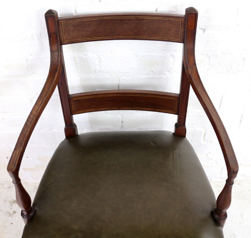 A set of twelve George III mahogany dining chairs featuring rectangular bar-back cresting rails with string inlay, green leather upholstered seats with stud detailing, and turned front legs. View XXVI