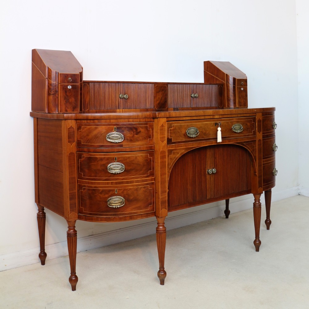 A George III Scottish flame mahogany stage-back sideboard featuring curved side drawers, inlay details, central tambour cupboards, and slender turned legs. View II