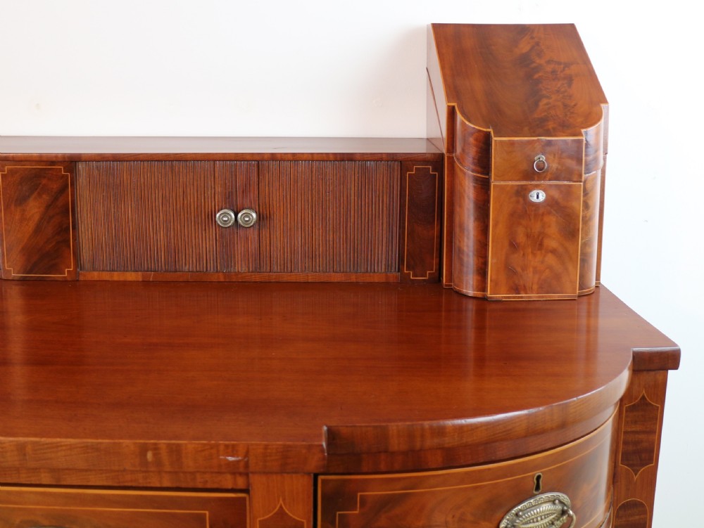 A George III Scottish flame mahogany stage-back sideboard featuring curved side drawers, inlay details, central tambour cupboards, and slender turned legs. View VII