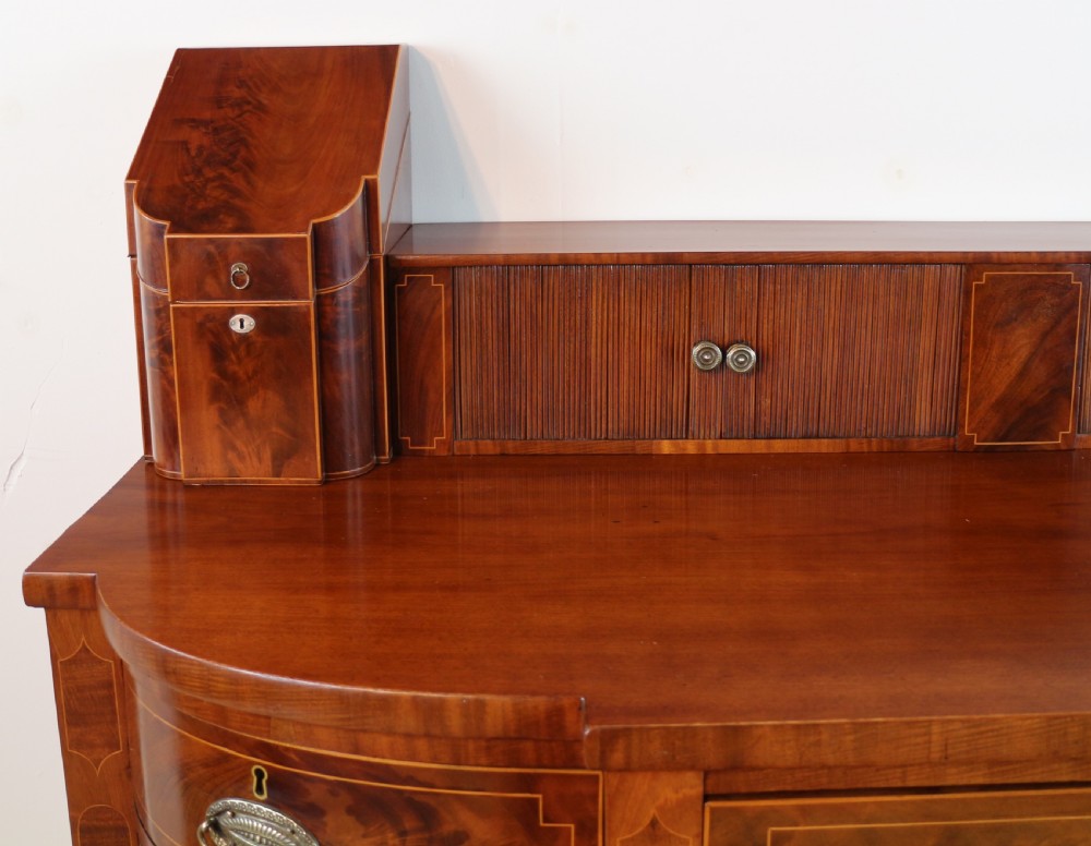 A George III Scottish flame mahogany stage-back sideboard featuring curved side drawers, inlay details, central tambour cupboards, and slender turned legs. View VIII