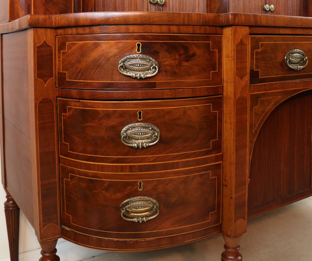 A George III Scottish flame mahogany stage-back sideboard featuring curved side drawers, inlay details, central tambour cupboards, and slender turned legs. View XI